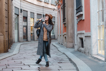 A young girl tourist in a fashionable brown hat is walking along a narrow street and taking pictures. Amid beautiful old buildings.