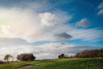 Fototapeta na wymiar Green grass golf fields, a few trees, dramatic cloudy blue sky in South Yorkshire in the warm sunny spring day