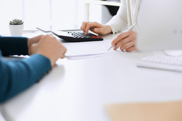 Accountant checking financial statement or counting by calculator income for tax form, hands closeup. Business woman sitting and working with colleague at the desk in office. Tax and Audit concept