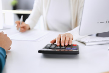 Accountant checking financial statement or counting by calculator income for tax form, hands closeup. Business woman sitting and working with colleague at the desk in office. Tax and Audit concept