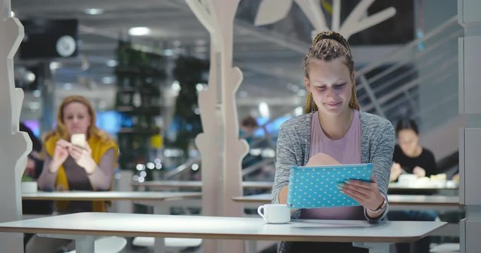 Young hipster female student surfing in internet using tablet PC sitting at city cafe food court. Attractive cute modern woman with dreadlocks using social networks