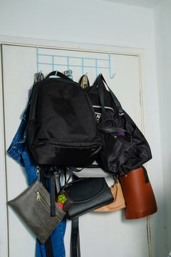 Collection Of Multiple Backpacks, Handbags And A Pair Of Jeans Stacked And Hanging On A Rack Behind The Door At Home.