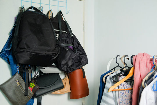 Collection Of Multiple Backpacks, Handbags And A Pair Of Jeans Stacked And Hanging On A Rack Behind The Door At Home.