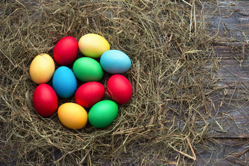Colorful easter eggs in straw nest on wooden background, rustic style, top view, space