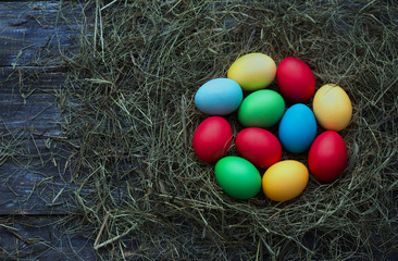 Fototapeta na wymiar Colorful easter eggs in straw nest on wooden background, rustic style, top view, space, toned