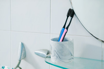 Couple blue and pink toothbrushes in ceramic mug in front of bathroom toilet mirror with reflection in the morning