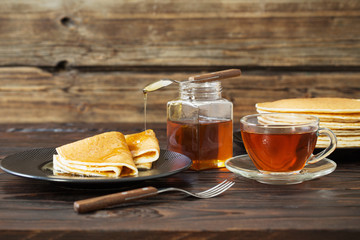 puncakes with honey and cup of tea on old wooden background