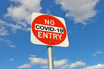 red, black and white No Entry COVID-19 warning sign on metal pole in blue sky background