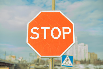 Obraz premium Stop sign - Red with white text with blue sky, clouds, buidings and pedestrian crossing sign in backgournd.