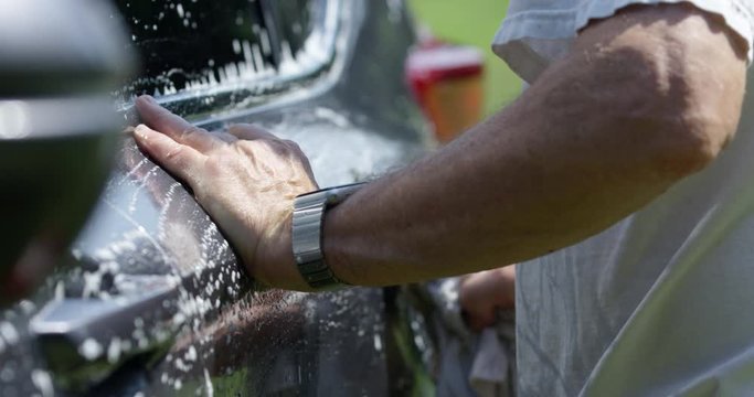 Man hand washing car outdoors in summer sun - close up as he applies soap to the side doors