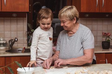 Little girl with grandmother in the kitchen sculpts dumplings