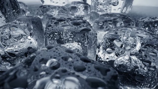 Melted ice cubes close up. Camera moves through ice cubes with water drops over dark background. UHD, 4K