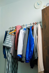 Collection of colorful clothes and jacket for male and female hanging on a rack by the window at home.