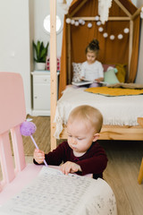 
The sisters play together in their large, sunny and bright room. They do not leave the house in self-isolation mode in an epidemic. Girl sitting on the bed and reading a book