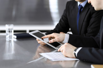 Businessman using tablet computer and work together with his colleague or partner at the glass desk in modern office, close-up. Unknown business people at meeting. Teamwork and partnership concept