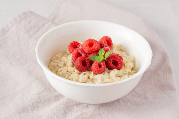 Oatmeal bowl with fresh raspberries and mint on grey napkin. Healthy breakfast. 