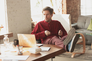 Fototapeta premium Watching serials. Caucasian entrepreneur, businessman, manager trying to work in office. Looks funny, lazy, spending time. Concept of work, finance, business, success and leadership. Deadline, hurry