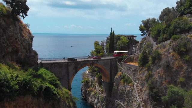 Aerial view inside bay of Fiordo di furore beach. Incredible beauty panorama of a mountains paradise. The rocky seashore of Italy. Sunny day. Stone bridge traffic, cars and motorcycle. Fast moving