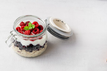 Overnight oatmeal with raspberries, blueberries, and yogurt in a jar isolated on grey background. Healthy vegetarian breakfast. Copy space. 