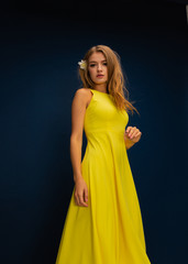 young beautiful  blonde girl in yellow summer dress and yellow shoes with flowers on blue studio background