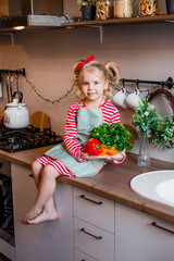 Little girl smiles sitting in the kitchen with vegetables for salad