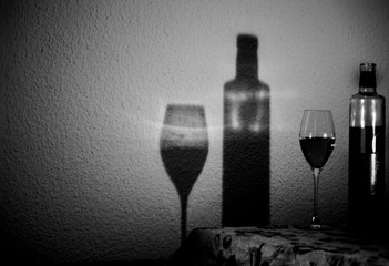 Still life of a bottle of wine and a glass served by casting its shadow on a stuccoed wall