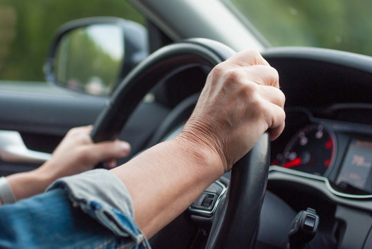 Middle aged woman driving car. Hands holding a steering wheel.