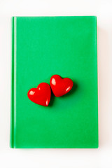two red hearts lying on green book over white isolated background like romantic book, love for reading, romantic reading and ecology book concept 