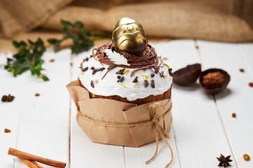 Easter cake decorated by golden chocolate egg on white wooden background, Traditional Kulich, Paska  ready for celebration