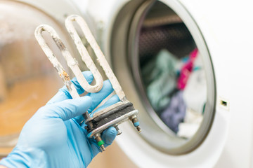 Washing machine repair. Hand of repairer with turbular electric heating element
