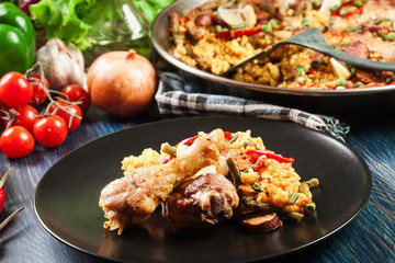 Traditional paella with chicken legs, sausage chorizo and vegetables served on black plate