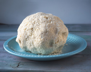 Curd dough for cheesecakes or dumplings, the finished dough rolled up in the shape of a ball lies on a blue ceramic torrel