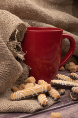 A red ceramic tea mug, cookie sticks with chocolate and white icing, and pieces of brown cane sugar...