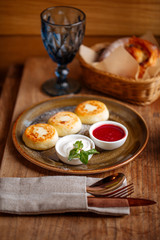 Fresh cooked sweet breakfast with cheese pancakes, sour cream and jam on the wooden table, vertical, side view