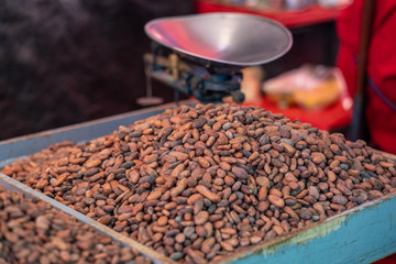Dried cocoa beans or cacao beans for sale in a market with a weighing scale in the background.