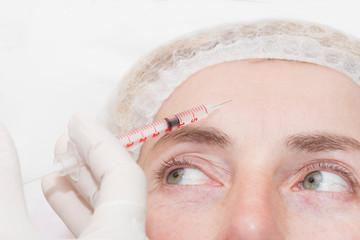 Cosmetic injection procedure in a beauty salon in the face of a woman of middle age.

