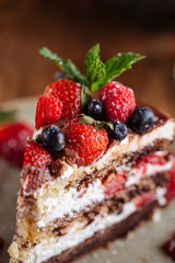 Fresh delicious piece of chocolate cake with strawberries, blueberries and mint, closeup, side view, vertical