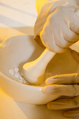 A chemist crushing tablets with a pestle and mortar.