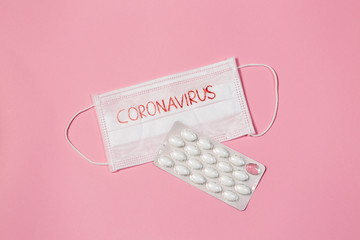 health and medicine. mask with text coronavirus and pills on pink background