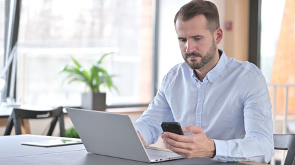 Young Man using Laptop and Smartphone in Office