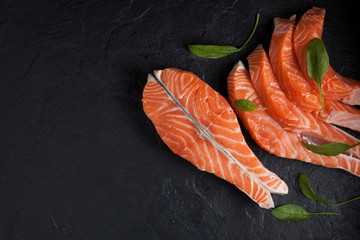 Steak and slices of salmon filet, decorated with spinach leaves on a black textured background. Close-up. Top view. Copy space