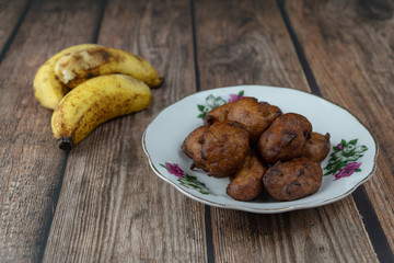 Popular Malaysian fritter snack deep fried banana balls or locally known as Cekodok Pisang in a plate over wooden background