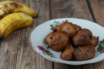 Popular Malaysian fritter snack deep fried banana balls or locally known as Cekodok Pisang in a plate over wooden background