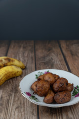 Popular Malaysian fritter snack deep fried banana balls or locally known as Cekodok Pisang in a plate over wooden background