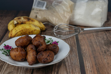 Popular Malaysian fritter snack deep fried banana balls or locally known as Cekodok Pisang in a plate over wooden background