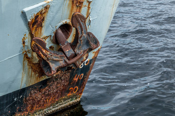 The rust anchor on the front of a gray steel ship. Ship is in the harbor