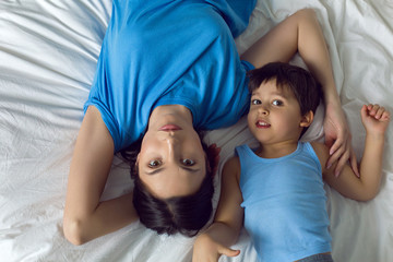 mother lies on a white bed with her son in the bedroom