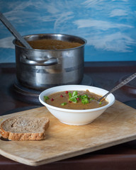 Homemade lentil soup puree with tomatoes. Plate with green onion soup in a white deep plate. In the background kkstrylya with soup ladle