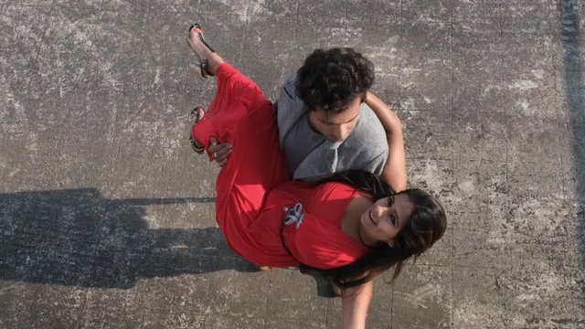 An young Indian Bengali brunette man in western wear taking his girlfriend moving in a slow circular motion on the rooftop. Indian lifestyle and holidays.