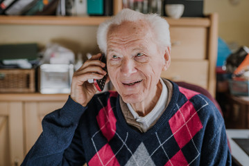 Elderly man talking on phone sitting at home